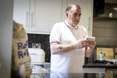 A man standing in his kitchen, reading something on his phone