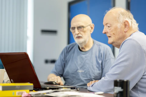 Two older men working something out together on a laptop