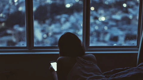 A woman by a window, looking at her phone