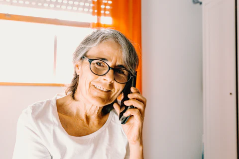 A woman in glasses listening carefully to a phone call at home